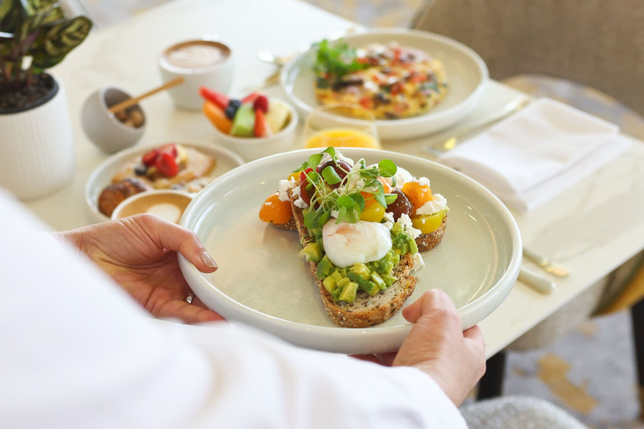 A person holding a plate with a sandwich topped with avocado, greens, and a poached egg.