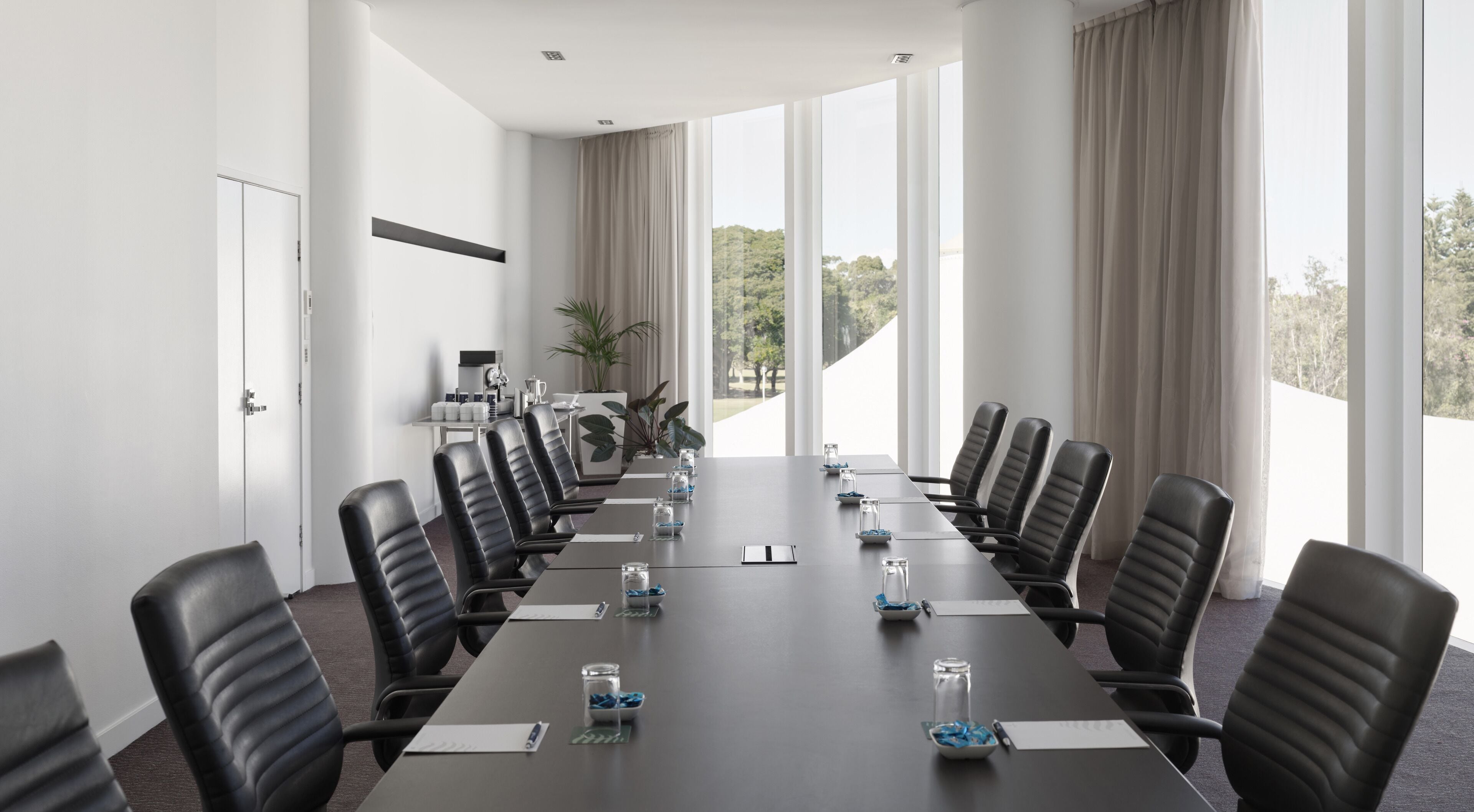 Una sala de conferencias con una larga mesa, varias sillas y ventanas amplias con cortinas.