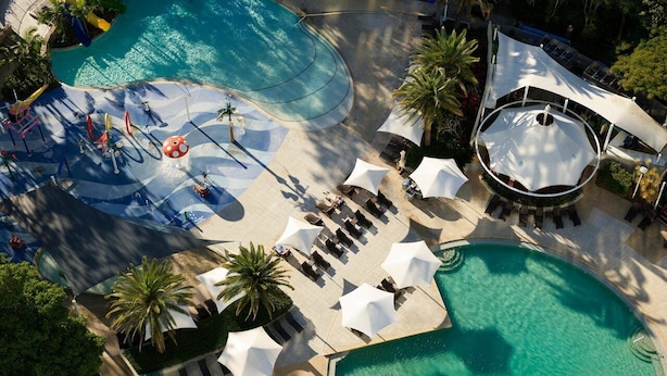 Vue aérienne d’un complexe hôtelier doté de plusieurs piscines, de chaises longues, de parasols et de palmiers.