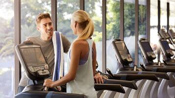 Un gimnasio con cintas de correr y una persona usándola.