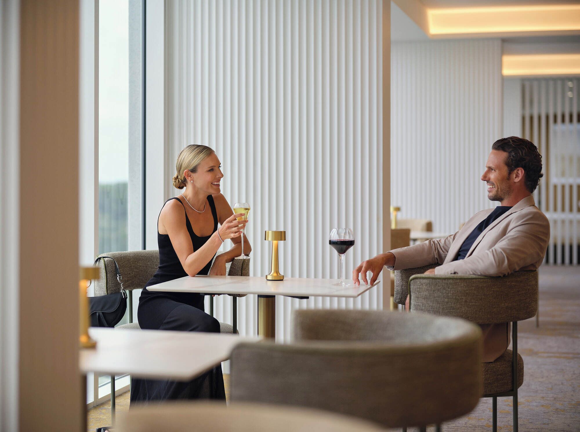 A modern hotel dining area with a table and chairs, a wine glass, and a decorative candle holder.