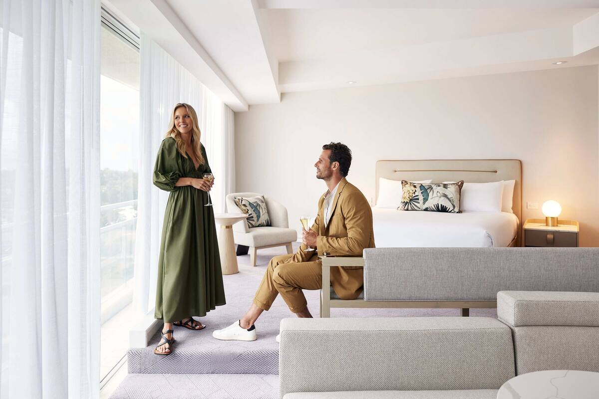 A modern hotel room with a large bed, a sofa, and a dining table.