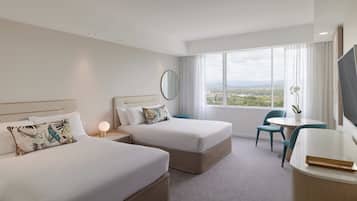 Habitación de hotel con dos camas, un escritorio, una silla, un ventanal con vistas y un espejo redondo en la pared.