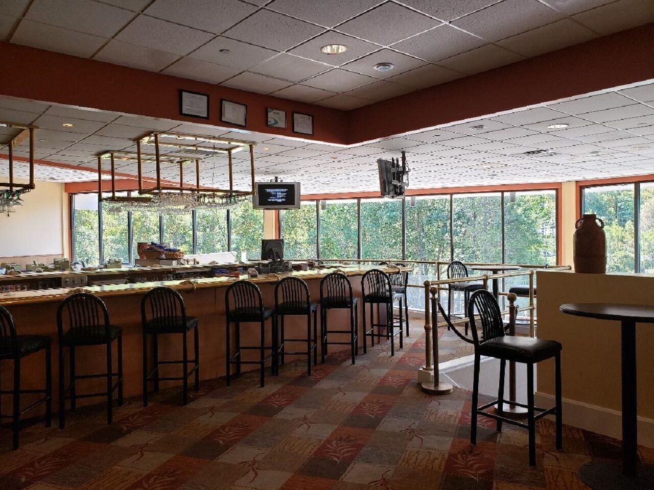 A restaurant with a bar area, multiple chairs, and large windows offering a view of trees.