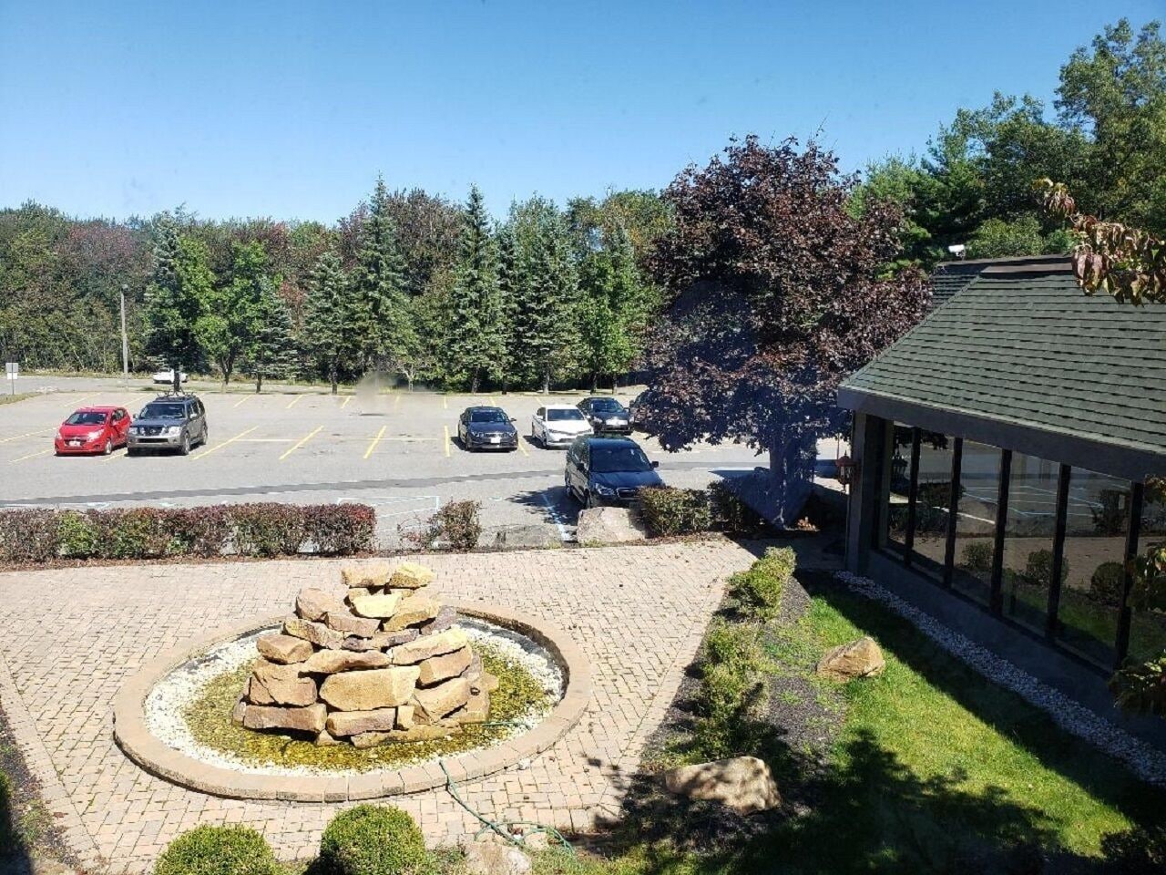 A parking lot with several cars, a stone feature in the foreground, and a building with large windows to the right.