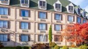 A multi-story hotel with a symmetrical facade, a central courtyard with a stone fountain, and a landscaped garden with autumn foliage. - Chateau Resort & Conference Center (Tannersville)