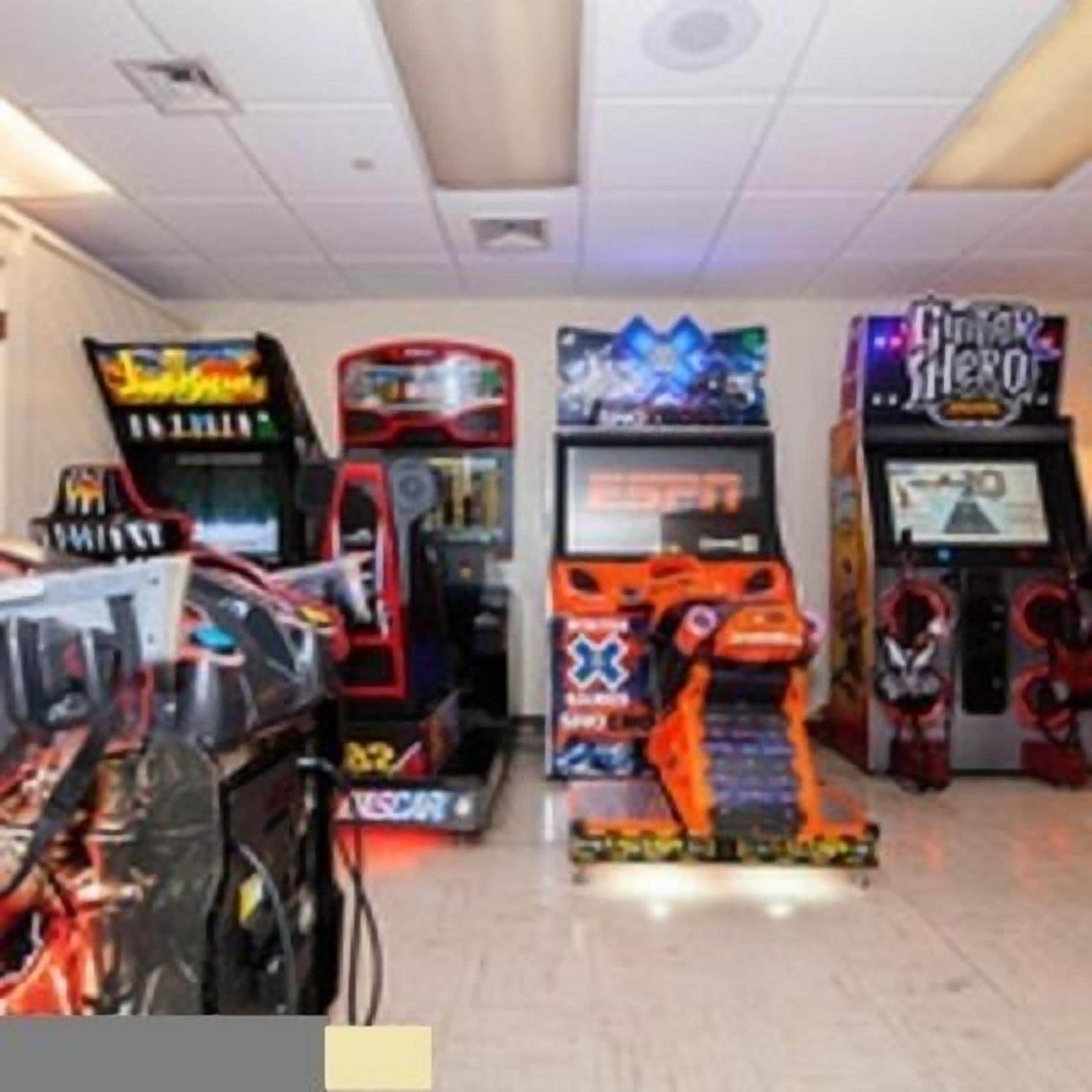 A row of arcade machines in a room with white walls and a tiled floor.