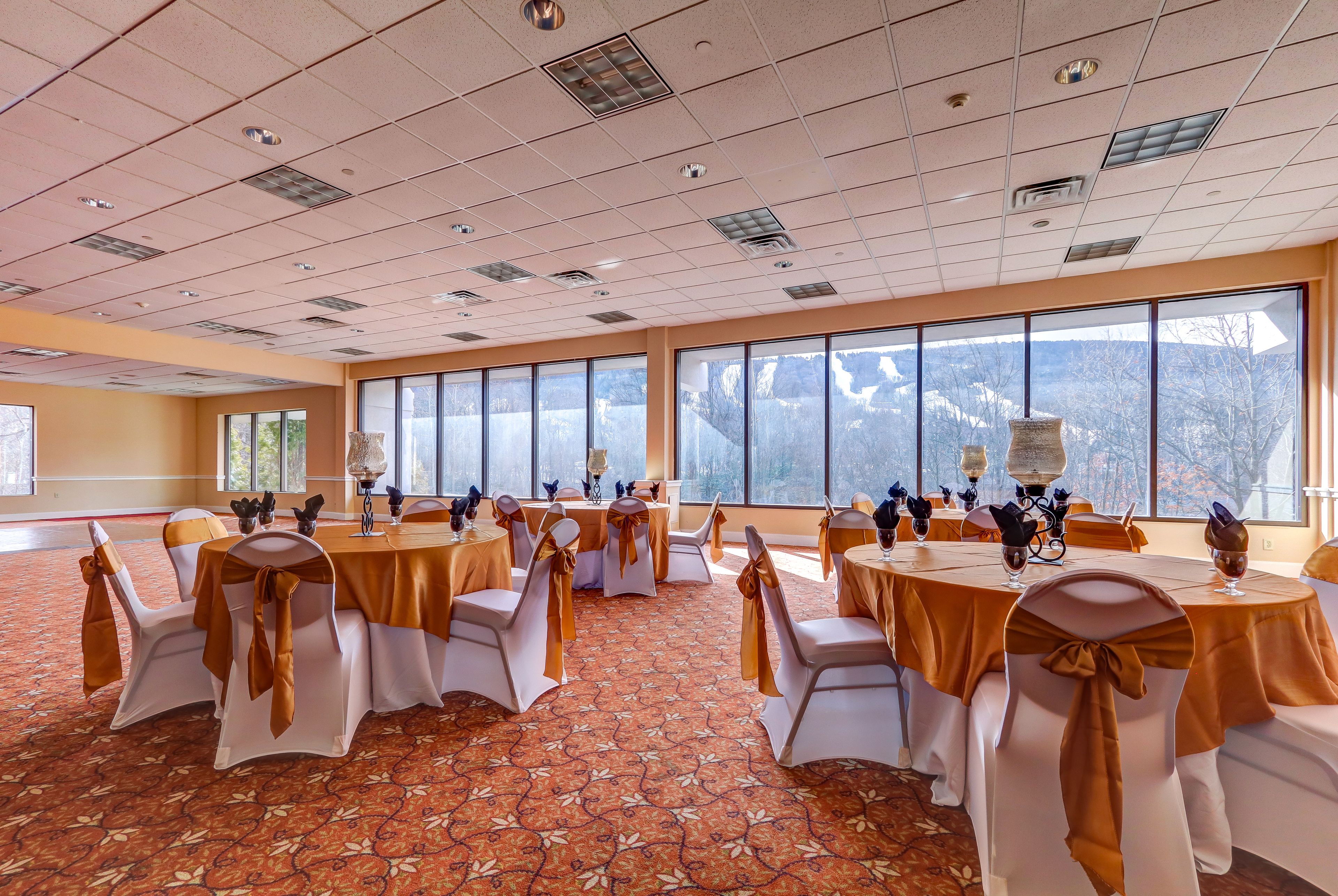A conference room with round tables, white chairs with orange sashes, and a carpeted floor.