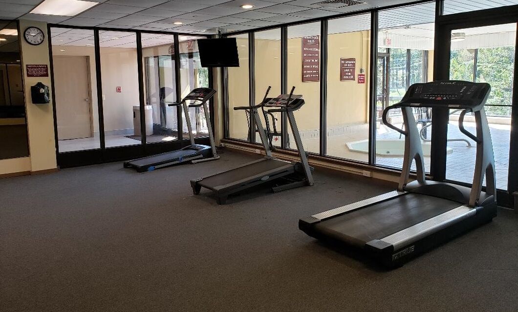 A fitness room with treadmills, a television, and a clock on the wall.