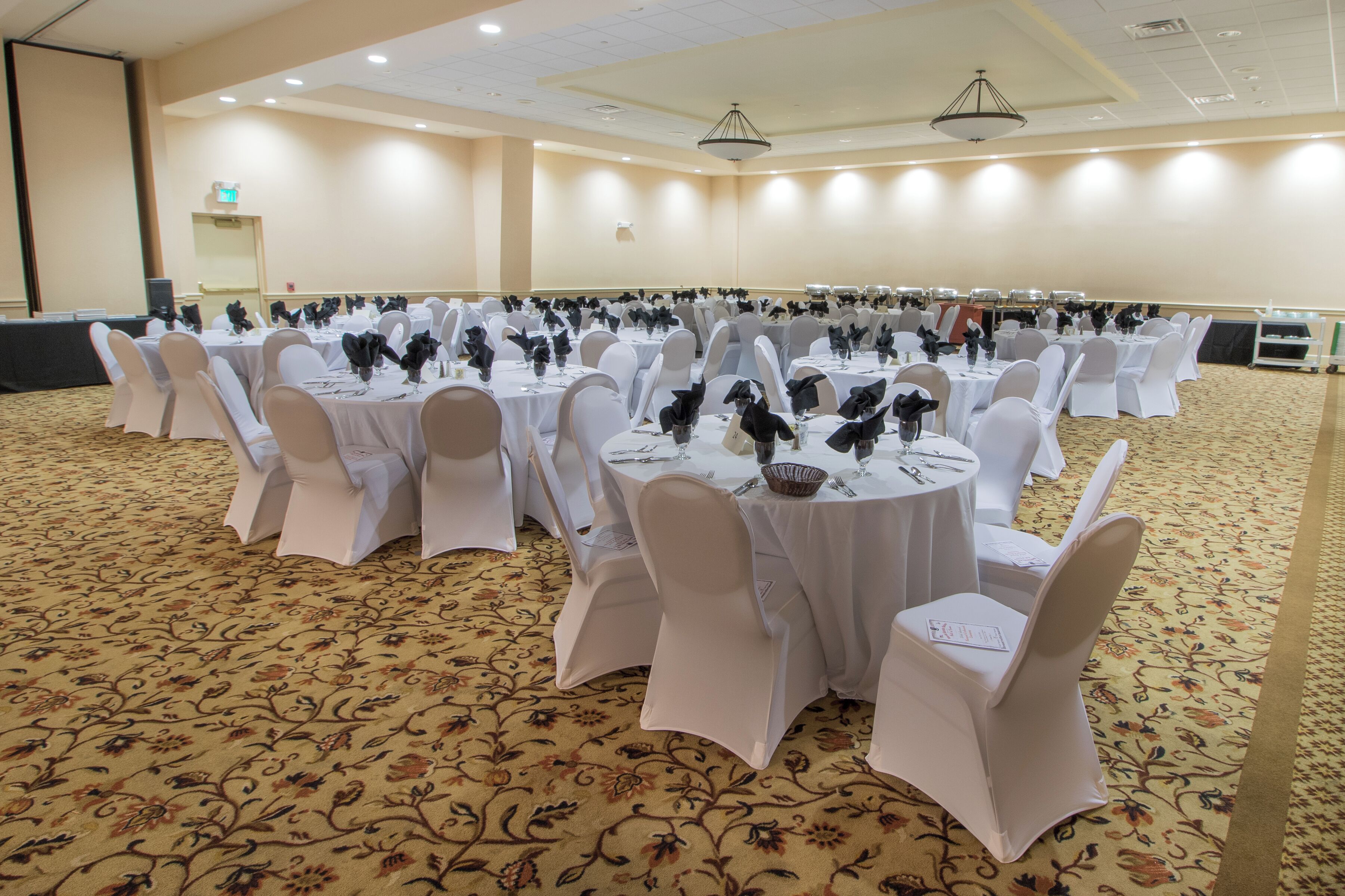 A banquet hall with round tables set with white tablecloths and chairs, arranged in rows.