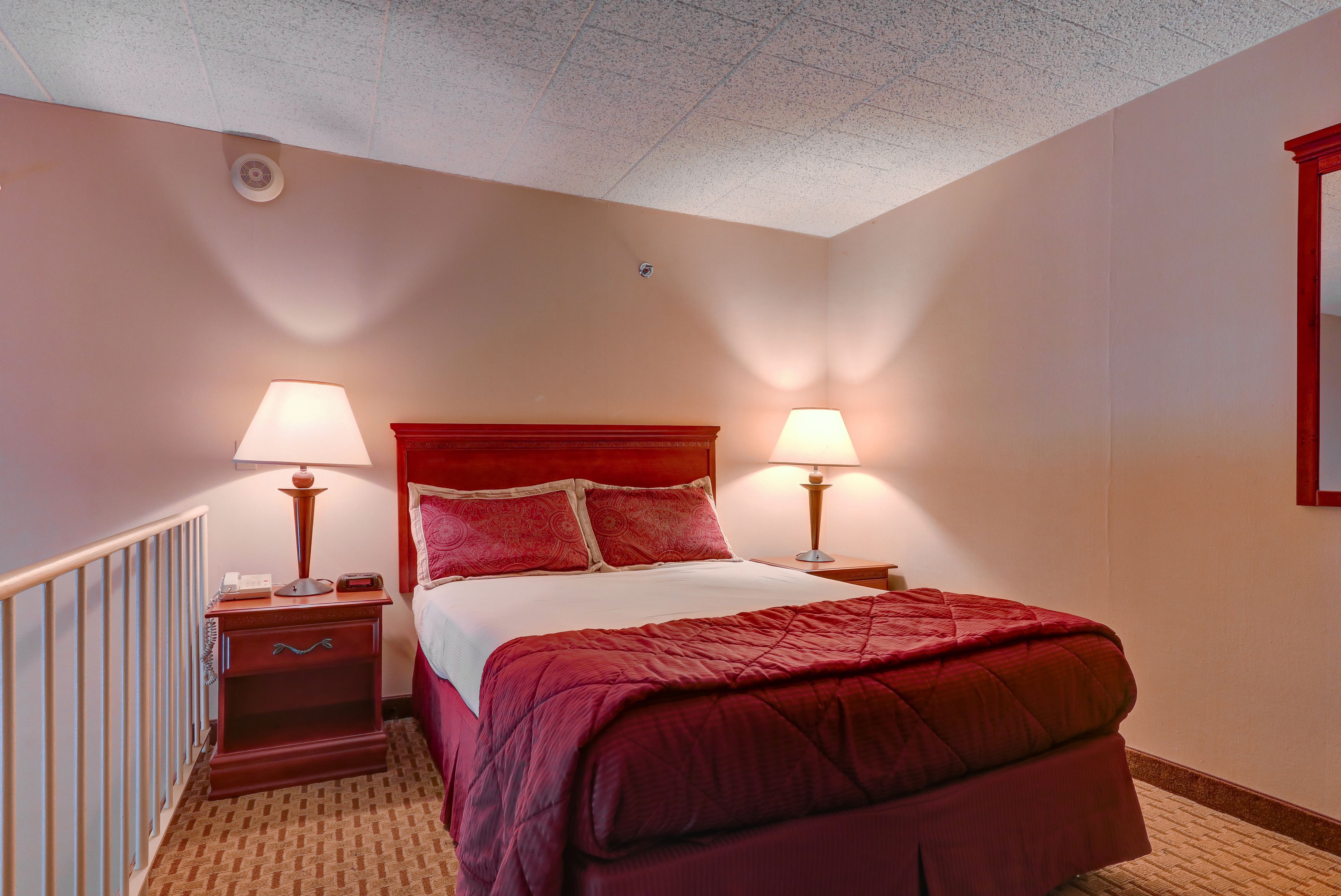 A hotel room with a large bed, two bedside tables with lamps, a red headboard, and a red carpet.