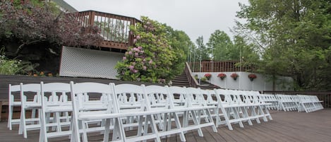 A wooden deck with white chairs arranged for an event.