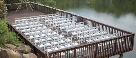 A wooden deck with white chairs arranged for an event.