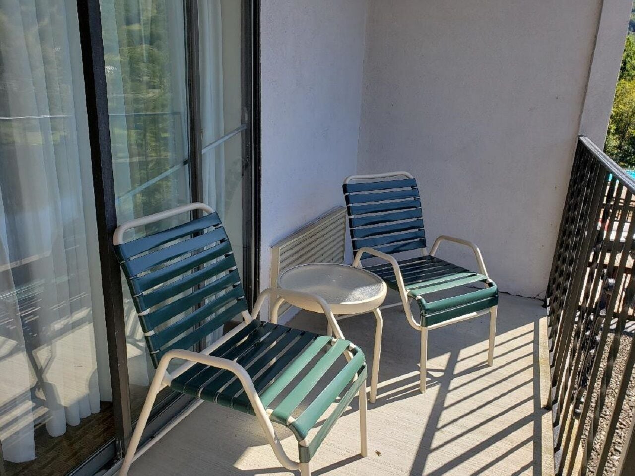Ein Balkon mit zwei grün-gestreiften Stühlen und einem kleinen runden Tisch.
