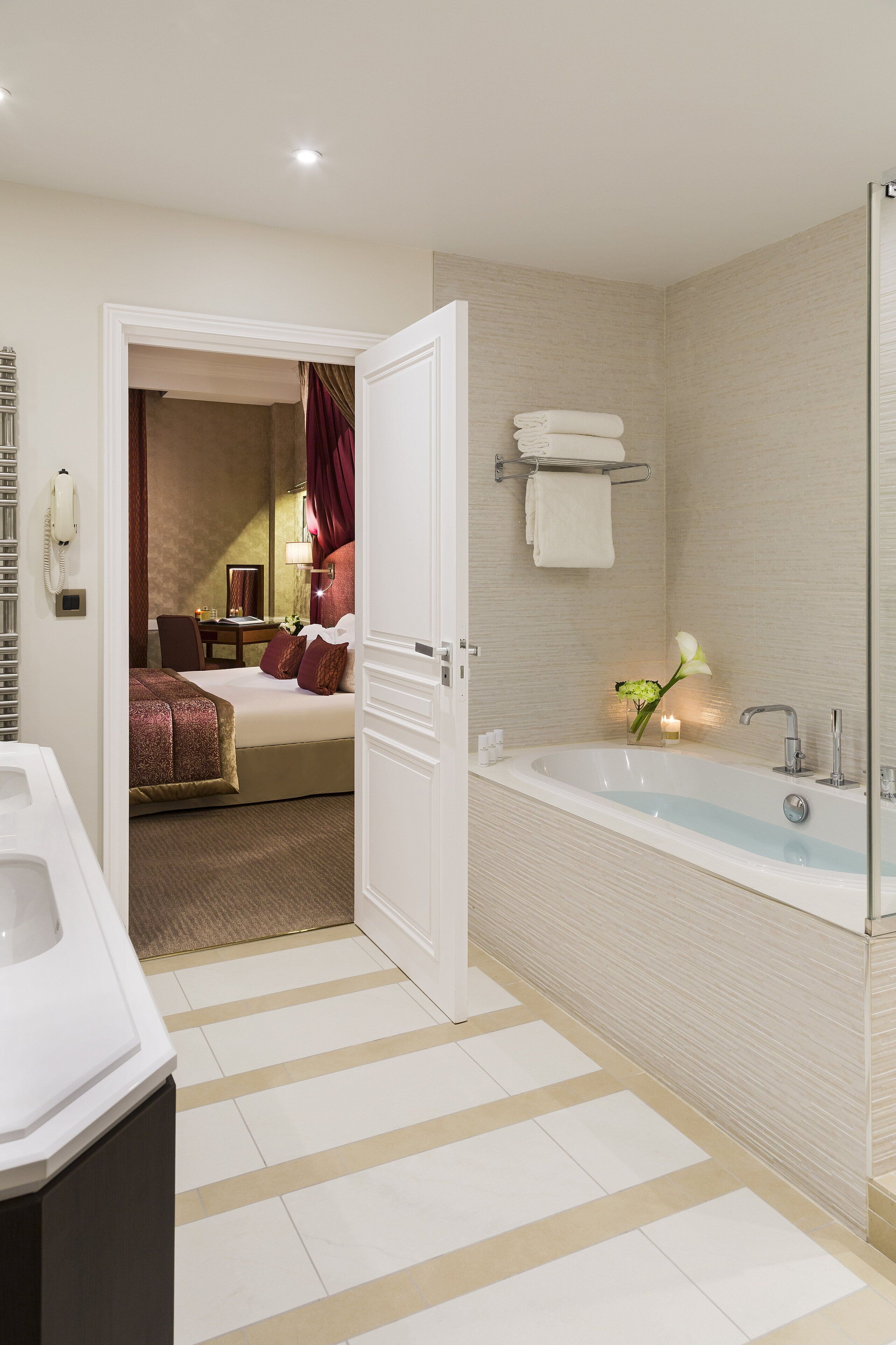 Une salle de bain d’hôtel dotée d’une grande baignoire, d’une douche séparée et d’une chambre visible avec un lit et un bureau.