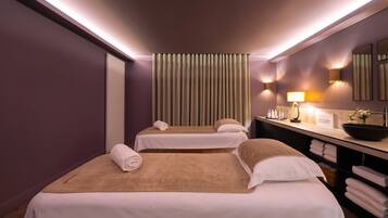 A hotel room with two beds, a large mirror, a vanity with a sink, and a window with vertical blinds.