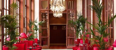 A hotel lobby with a grand chandelier, red seating, and tall windows.