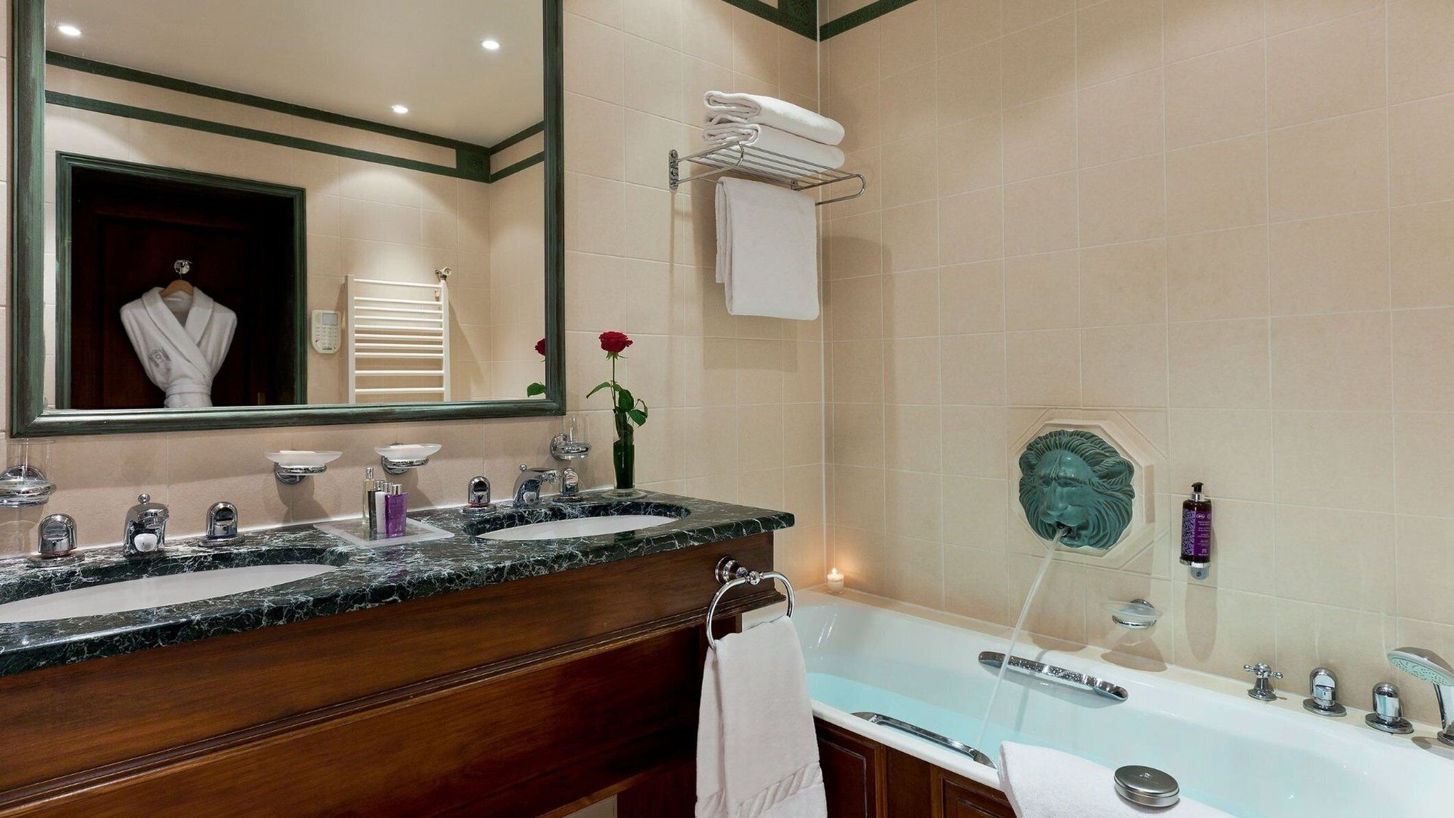 A bathroom with a double sink, a large mirror, a vanity with a marble countertop, a bathtub, and a wall-mounted towel rack.