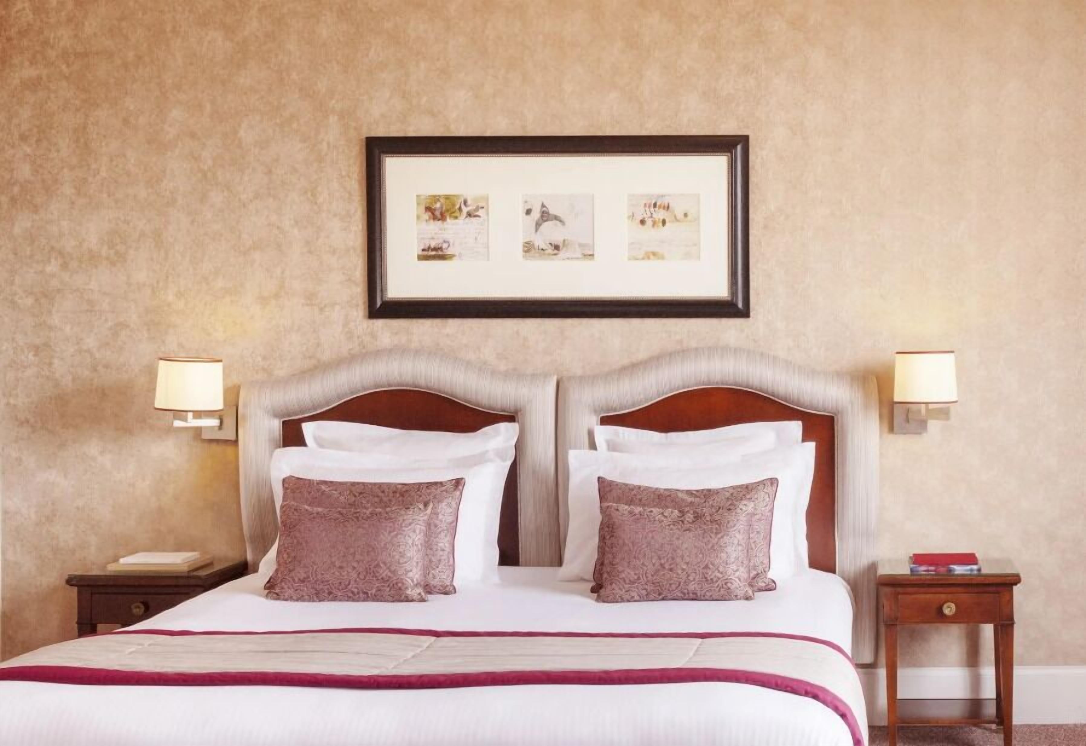 A neatly made bed with white and pink linens, two bedside tables with lamps, and a framed picture above the bed.