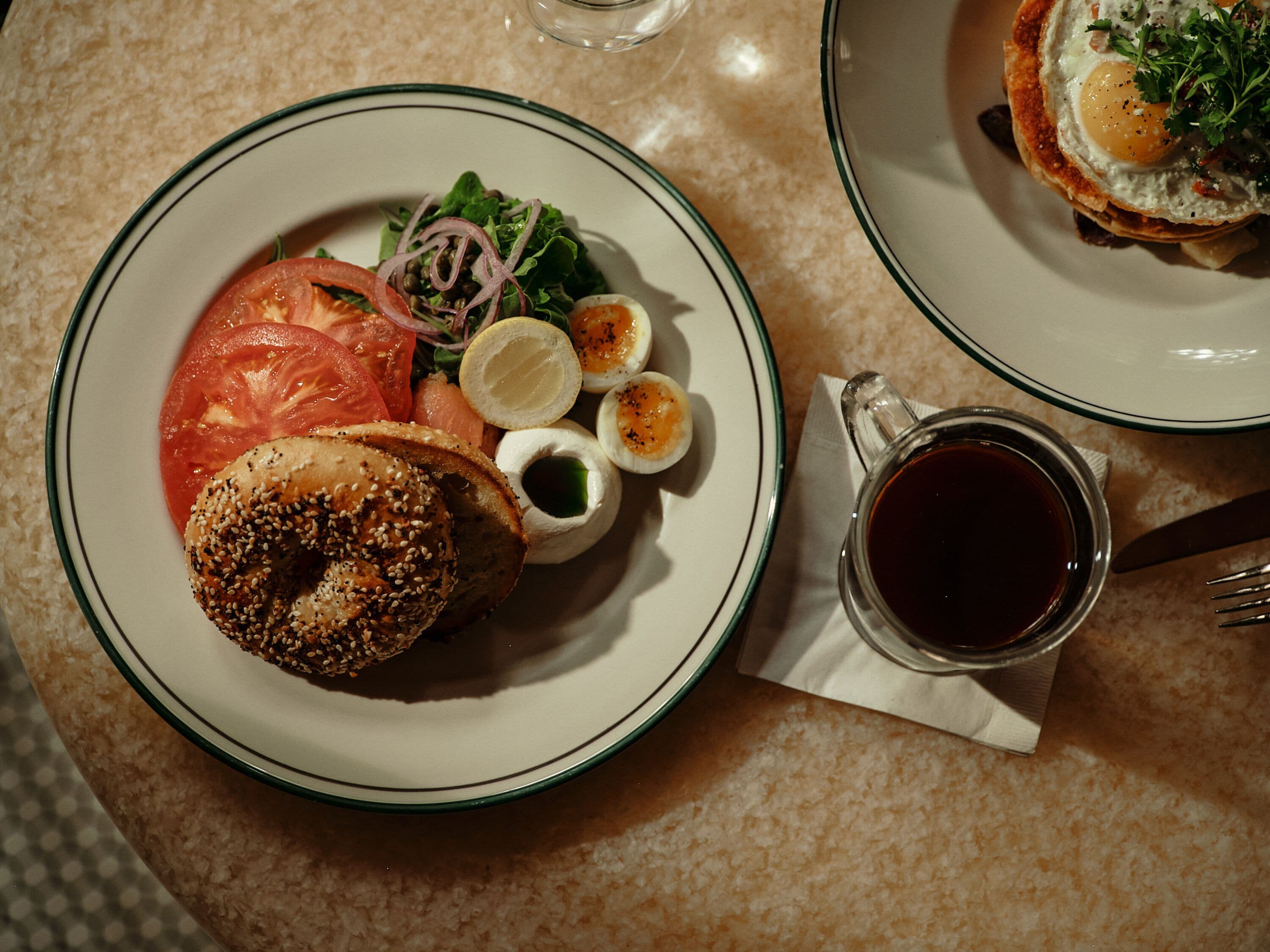 A plate with a bagel, tomatoes, onions, and boiled eggs on a table.