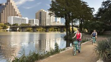 Een pad langs de rivier met fietsers, een brug en stadsgebouwen op de achtergrond.
