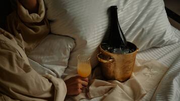 A person lying on a bed with a bottle of champagne and a glass of orange juice.