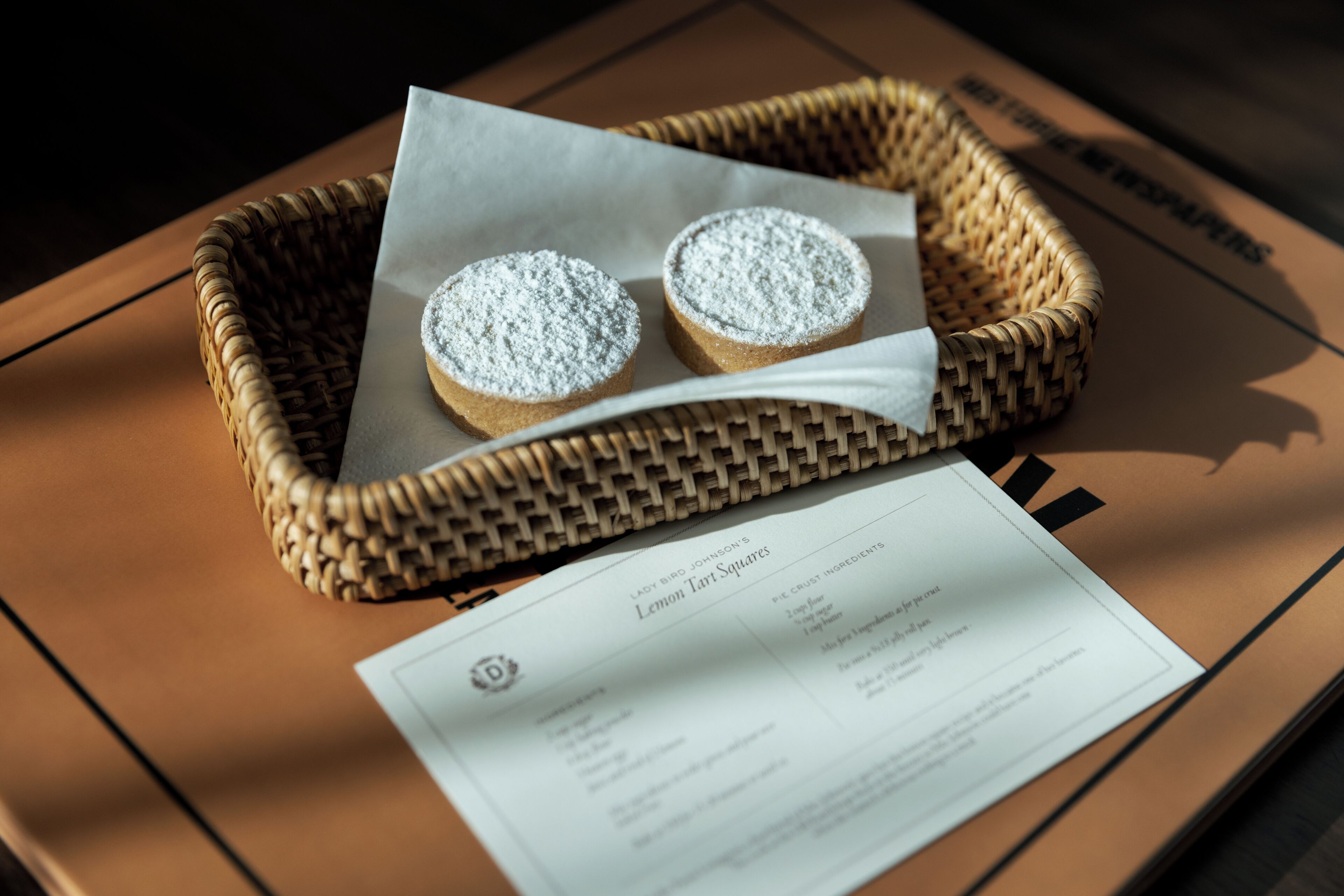 A wicker basket with two lemon tart squares on a brown surface.