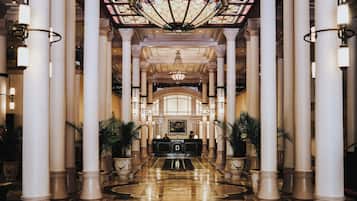 Un vestíbulo imponente con una recepción central, flanqueada por altas columnas y candelabros ornamentados.