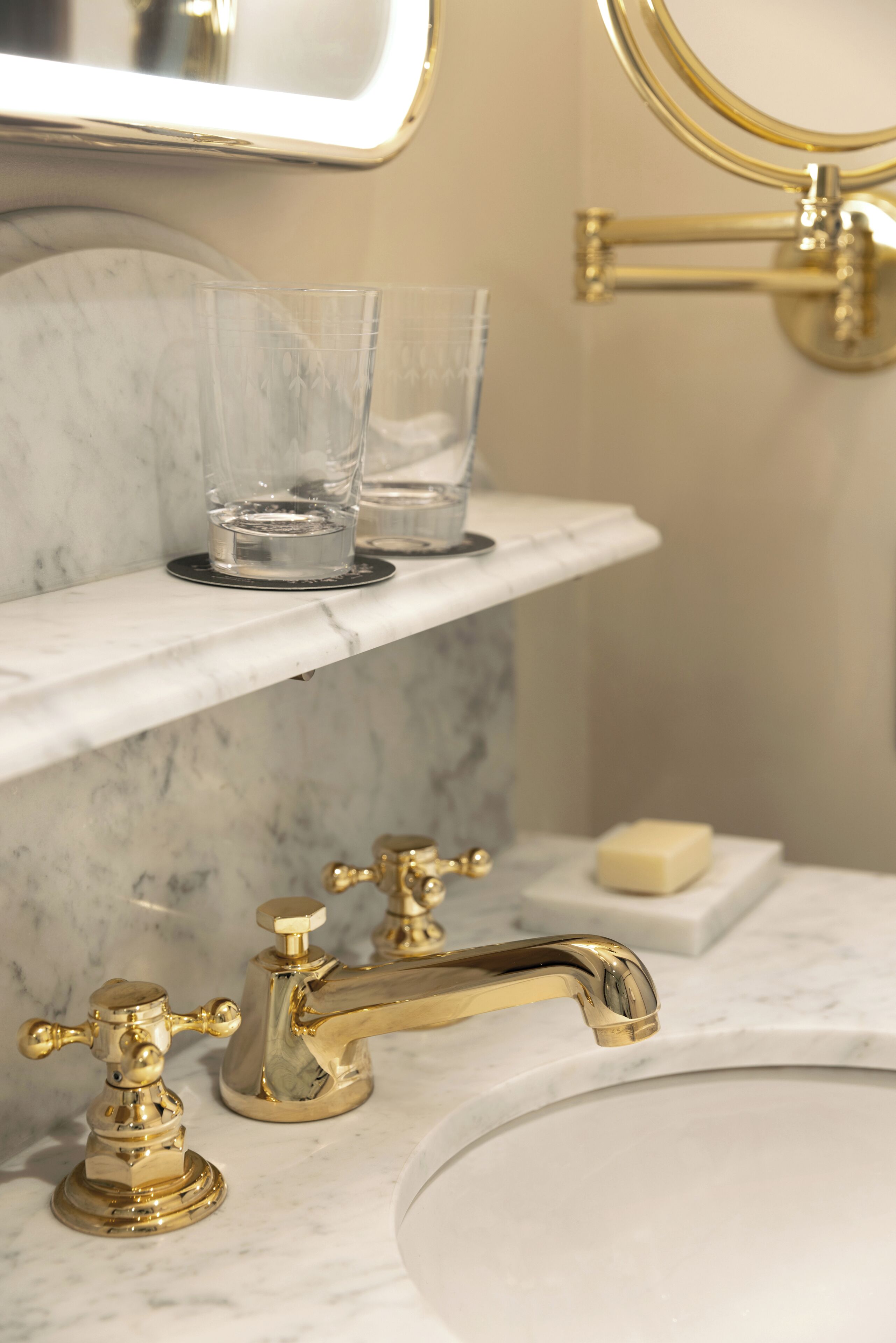 A bathroom with a marble sink, gold faucets, a mirror, and a glass on the countertop.