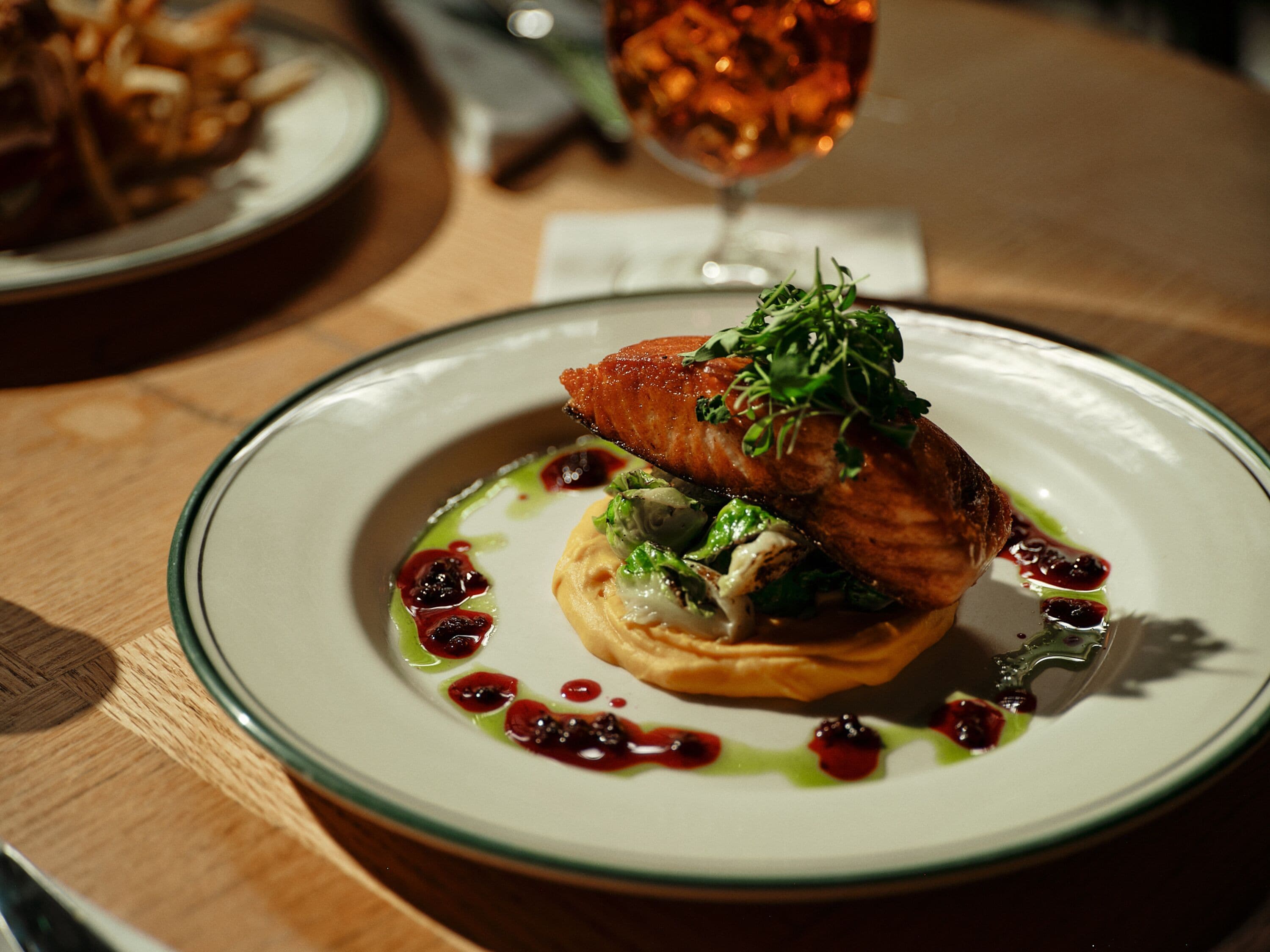 Une assiette de nourriture comprenant un morceau de saumon, des légumes verts et de la sauce, le tout présenté sur une assiette blanche.