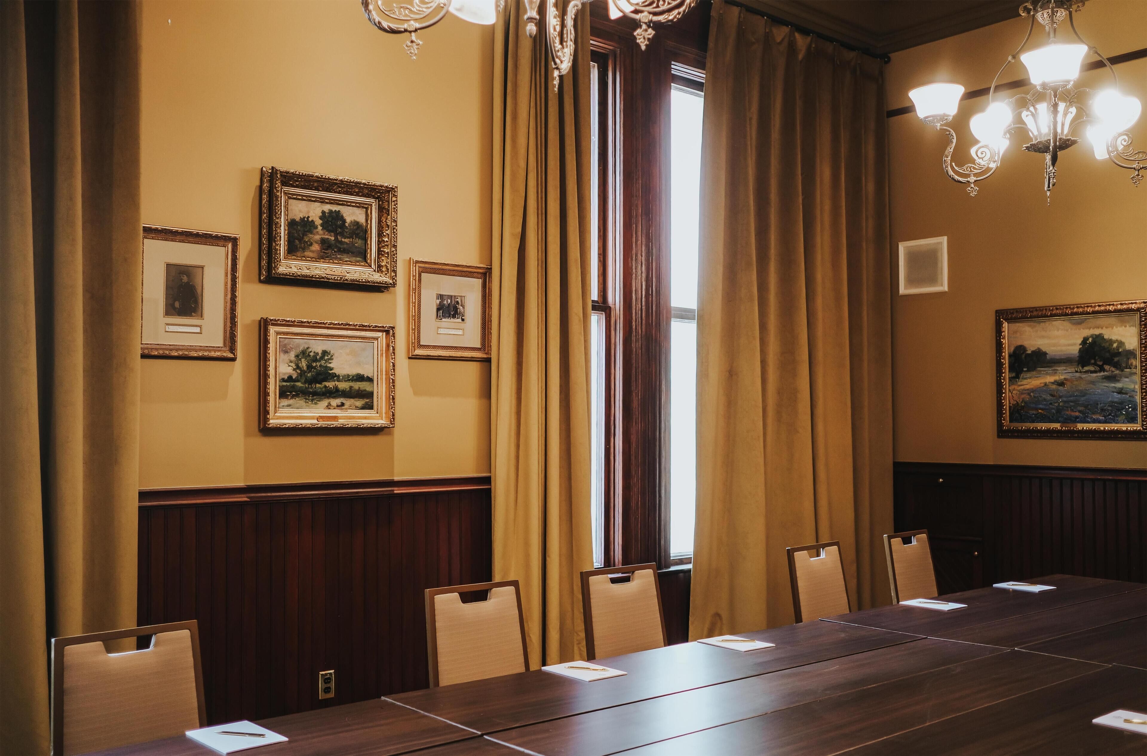 A conference room with a long table, chairs, framed pictures on the walls, and a chandelier.