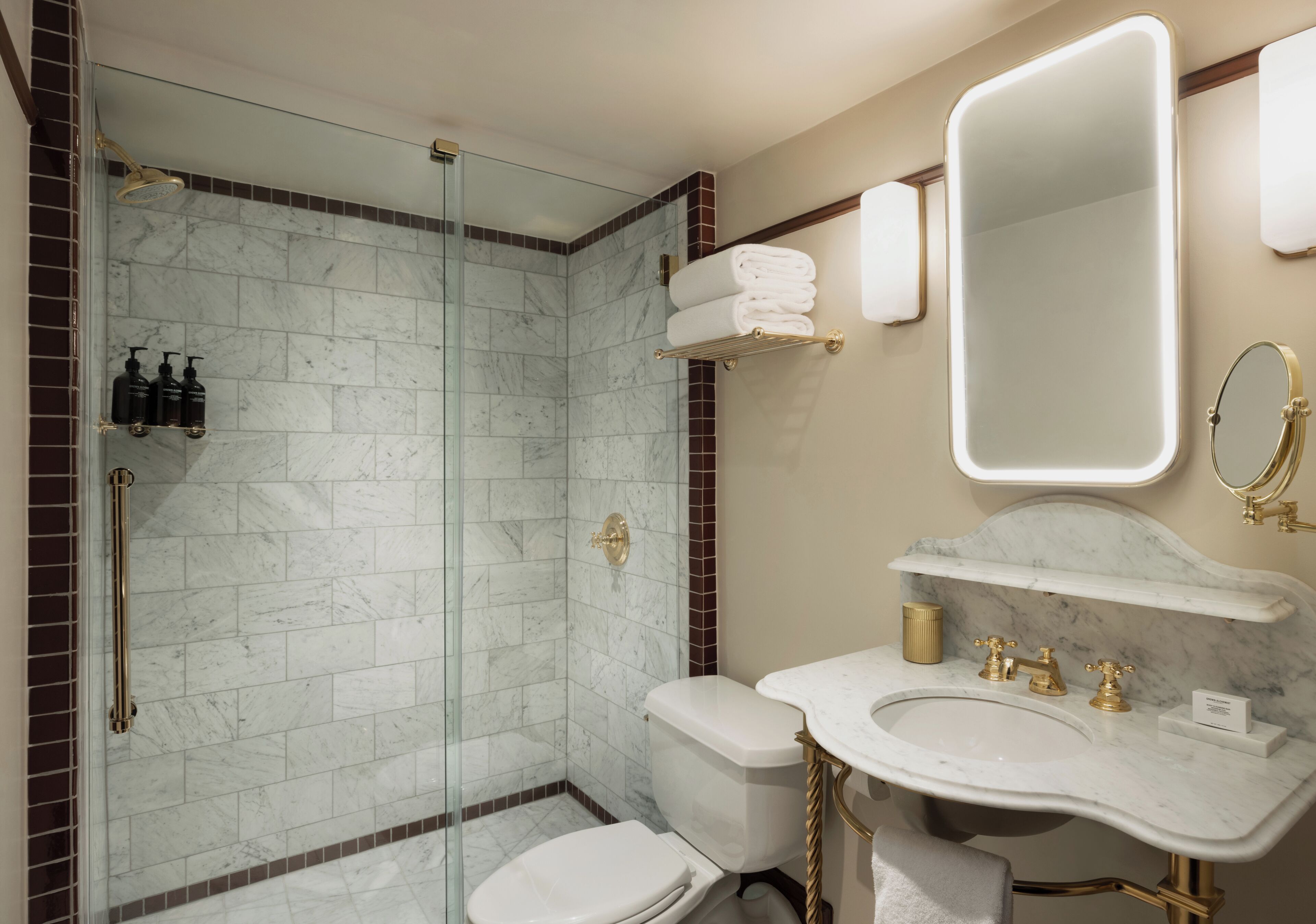 A bathroom with a glass-enclosed shower, a toilet, a sink with gold fixtures, and a large mirror.