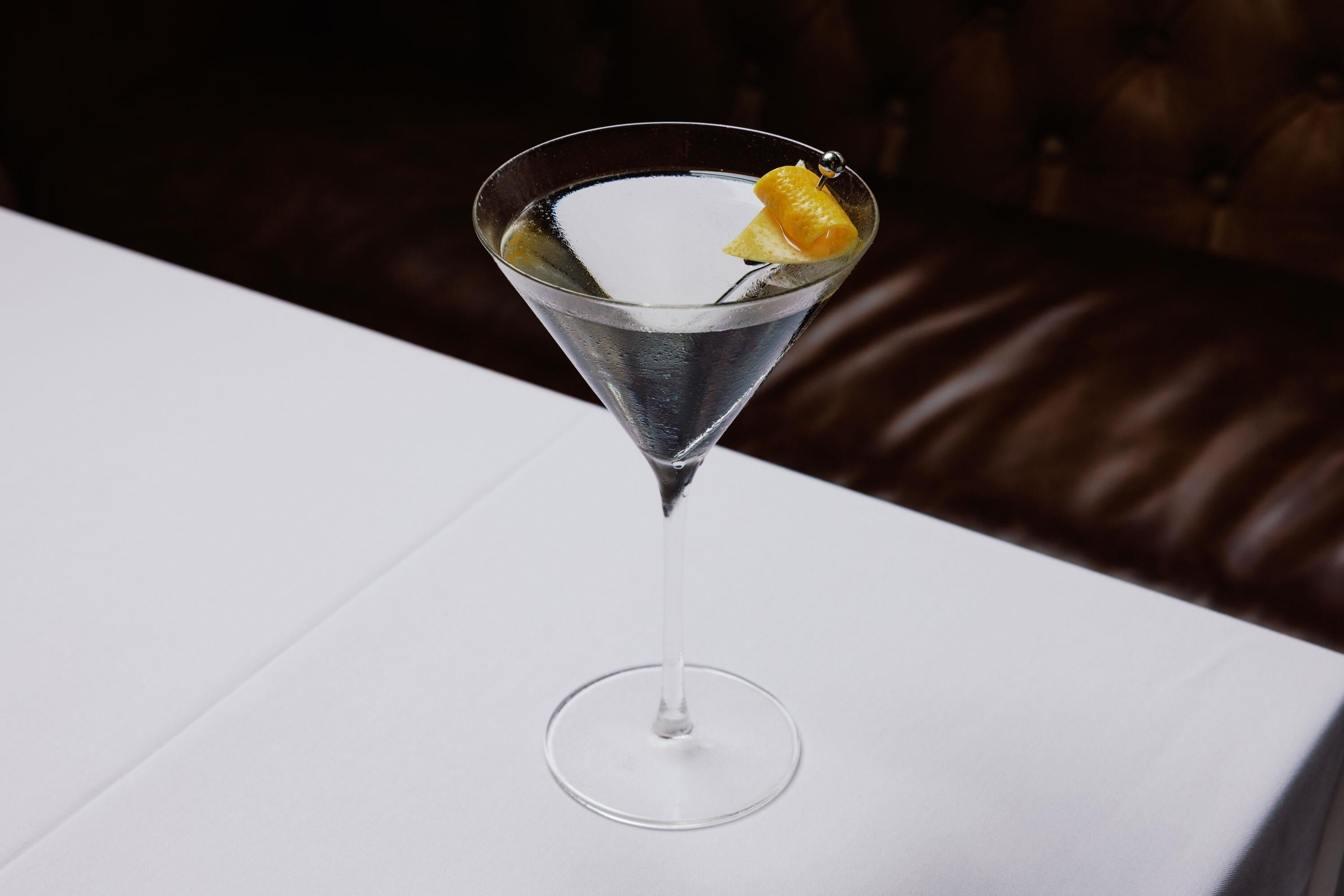 A martini glass with a lemon twist on a white table.
