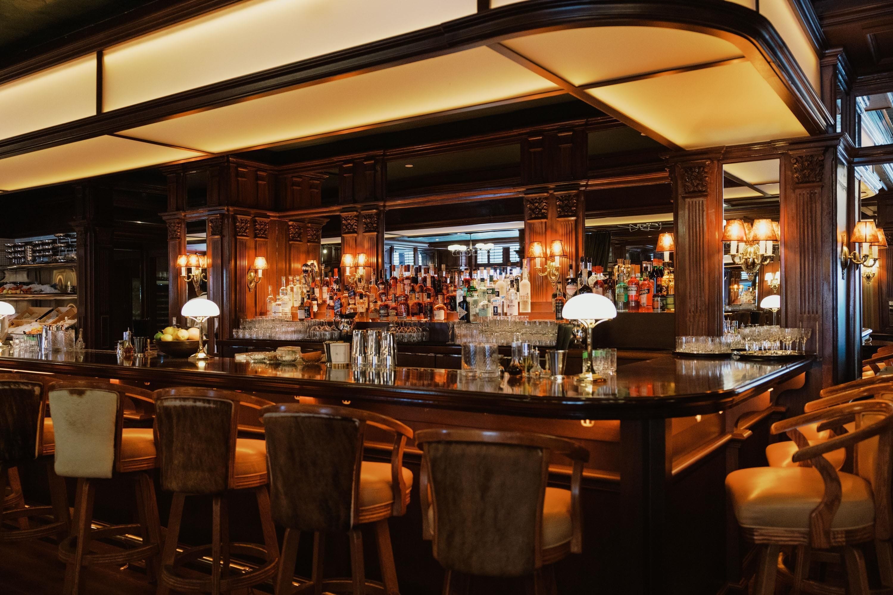 Un área de bar con taburetes de madera, una barra bien surtida y lámparas decorativas.