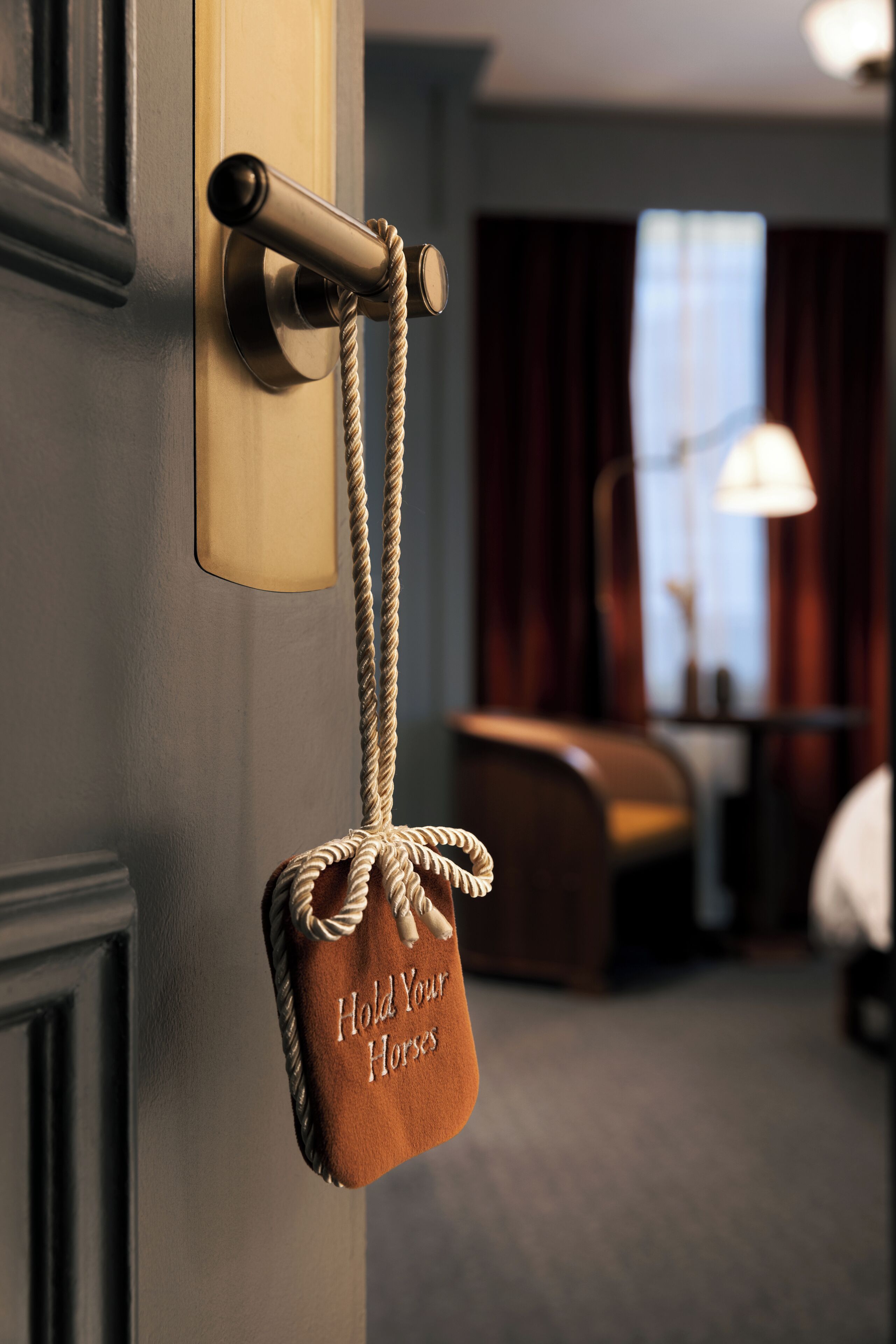 A door with a rope handle and a sign that reads 'Hold Your Horses.'