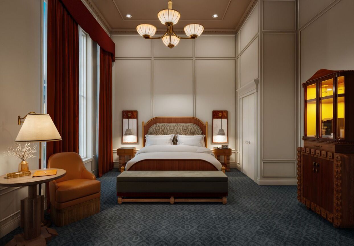 Una habitación de hotel con una cama grande, un escritorio con lámpara, una silla, un armario y una araña.