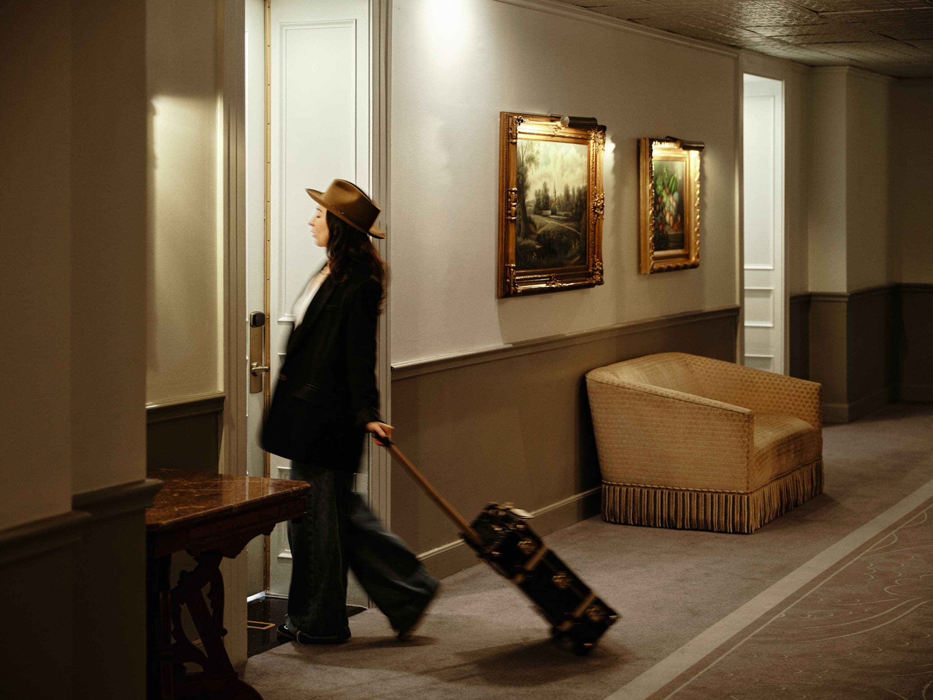 A hallway with a wooden bench, a door, and two framed paintings on the wall.