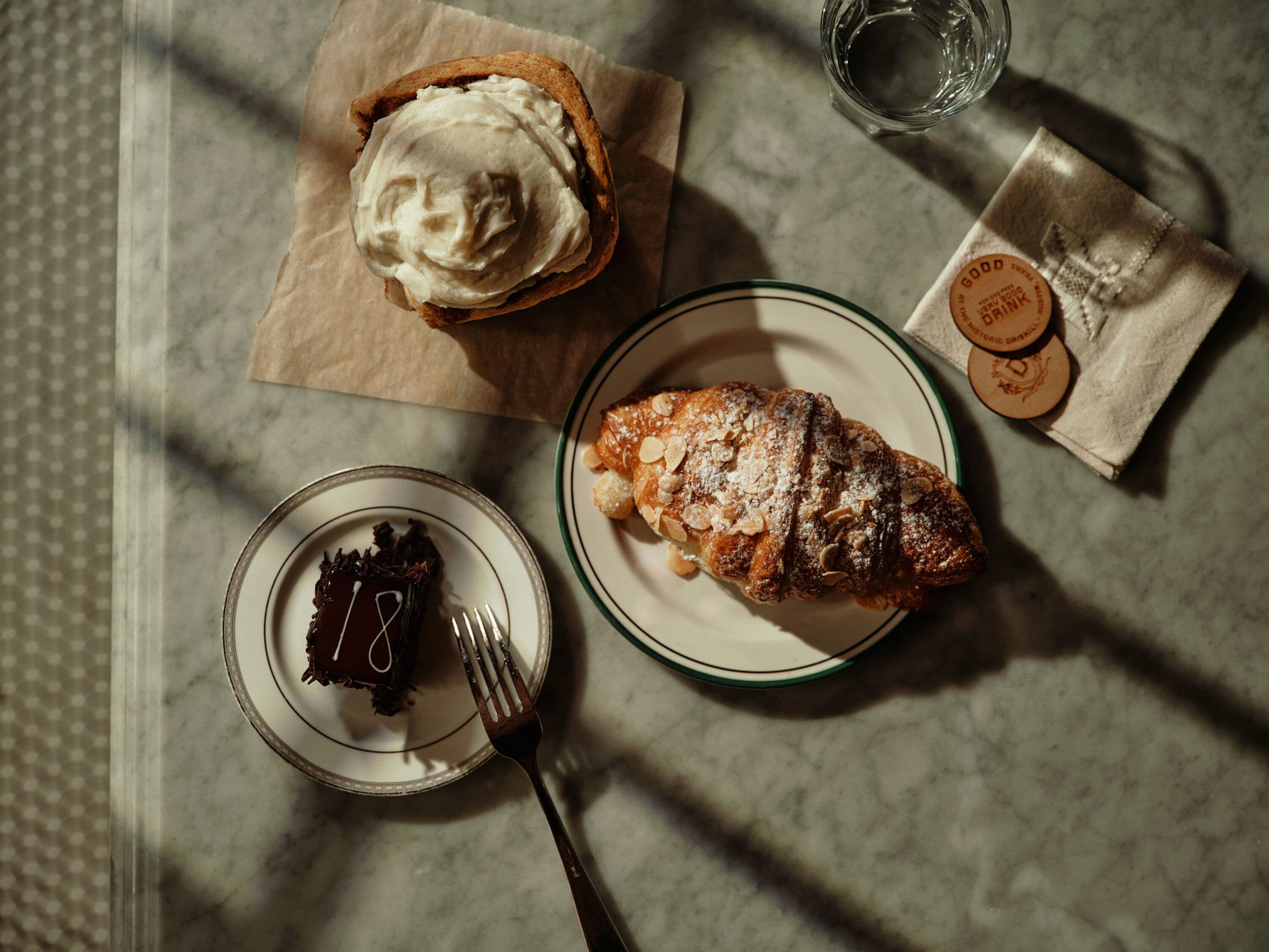 A dessert plate with a pastry, a slice of cake, and a glass of water on a marble table.