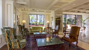 A spacious lobby with a green sofa, patterned armchairs, a coffee table, and a large window offering a view of the outdoors.