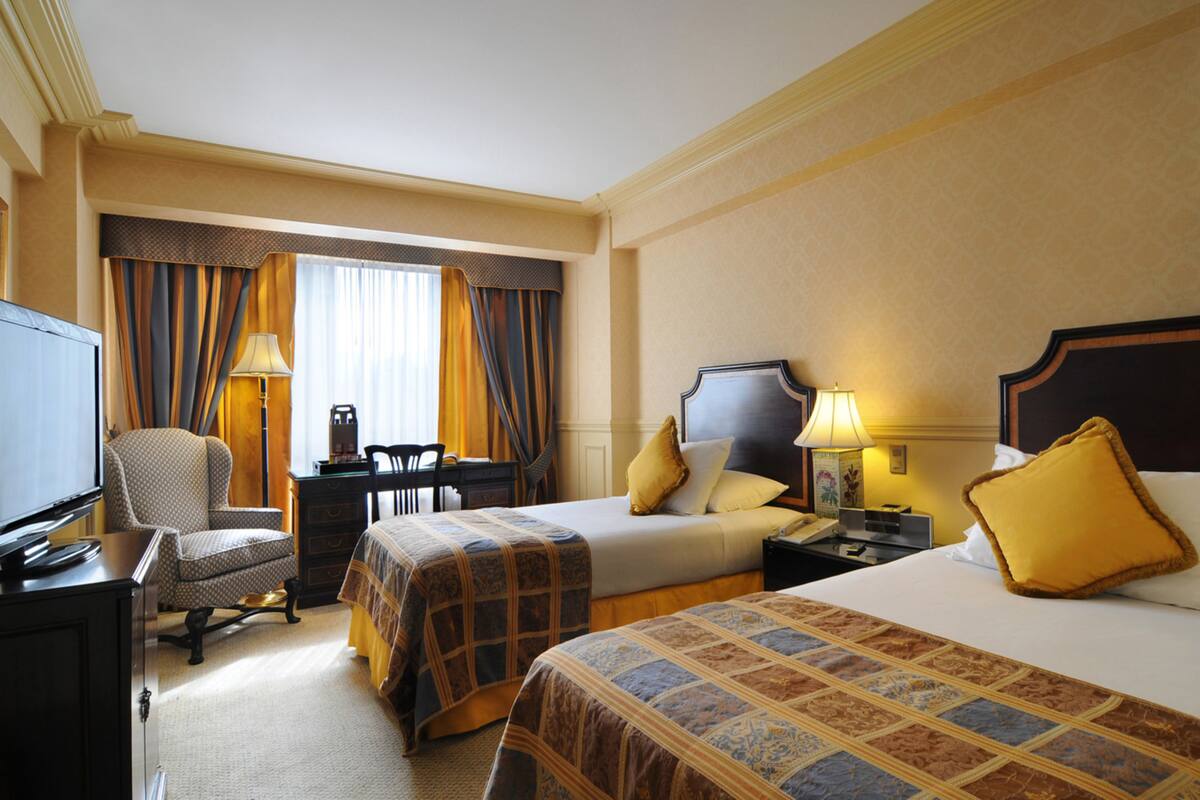 Hotelkamer met twee bedden, een bureau, een stoel, een televisie en een raam met gordijnen.