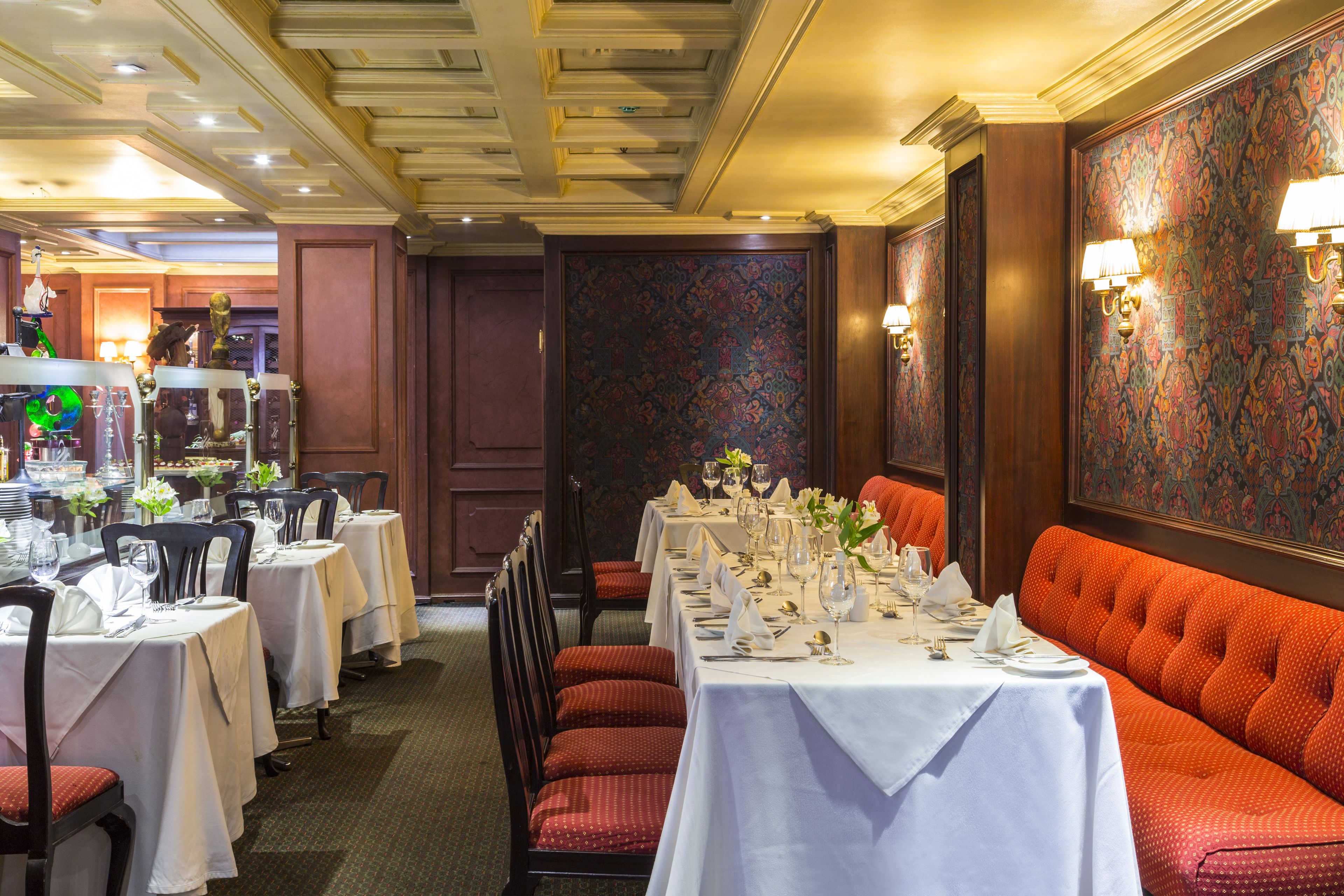 A restaurant with multiple tables set for dining, featuring a mix of red and white upholstered chairs.