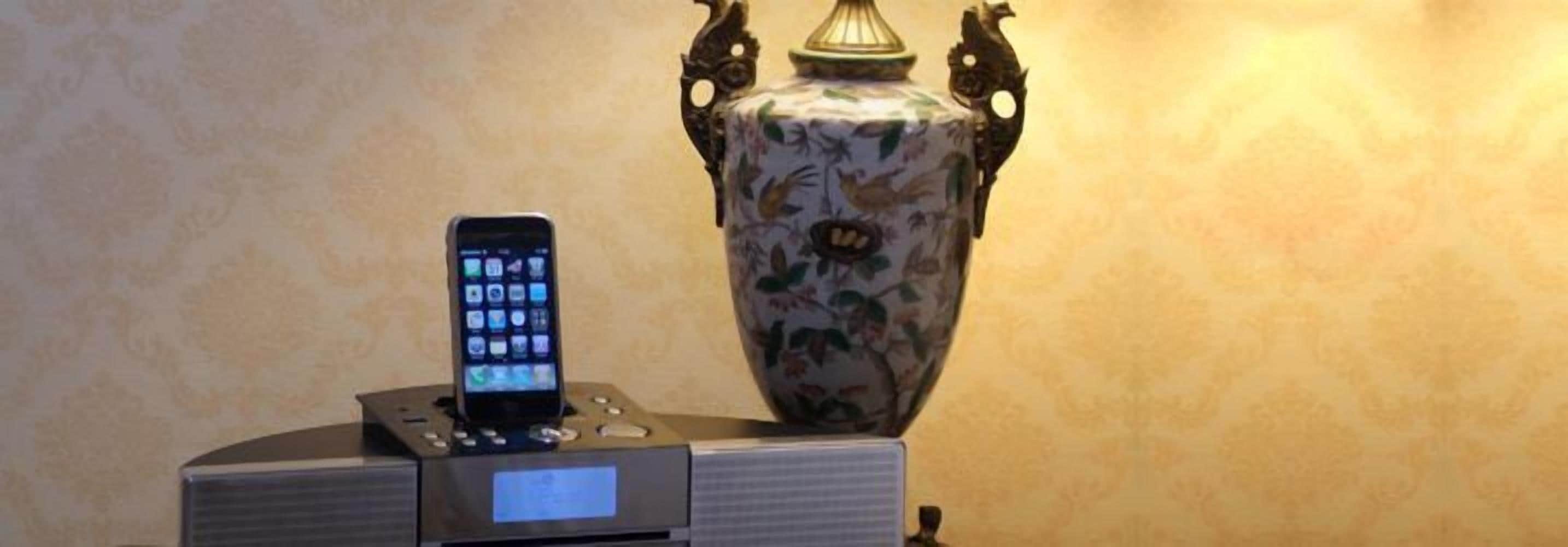 Un teléfono inteligente en una base de carga, un jarrón decorativo y una pequeña mesa con una lámpara.