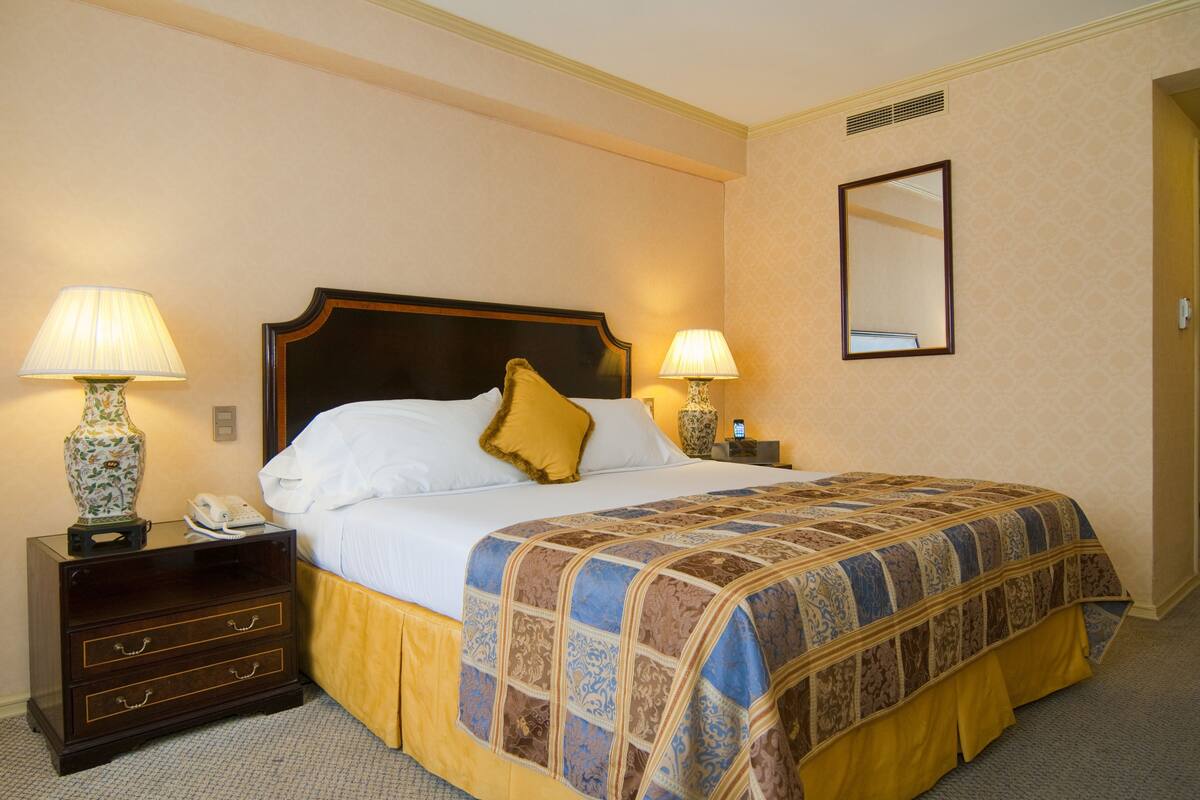 Een hotelkamer met een groot bed, twee bedlampjes, een nachtkastje met een telefoon en een spiegel aan de muur.