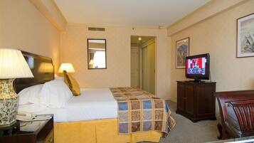 A hotel room with a bed, a television, a lamp, a mirror, and a door leading to another room.
