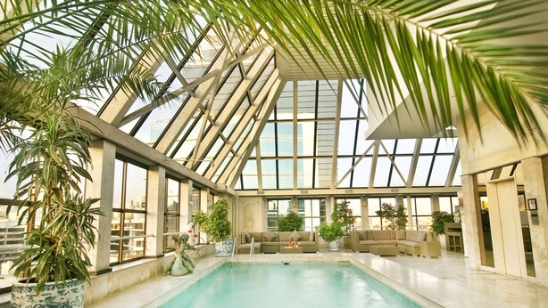 An indoor swimming pool with a high ceiling, large windows, and multiple seating areas.