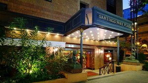 The exterior of Santiago Park Plaza hotel with a covered entrance, a statue, and well-lit surroundings.