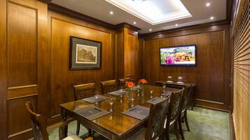 Un salón de conferencias con una larga mesa de madera, sillas y un televisor en la pared.