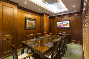 Un salón de conferencias con una larga mesa de madera, sillas y un televisor en la pared.