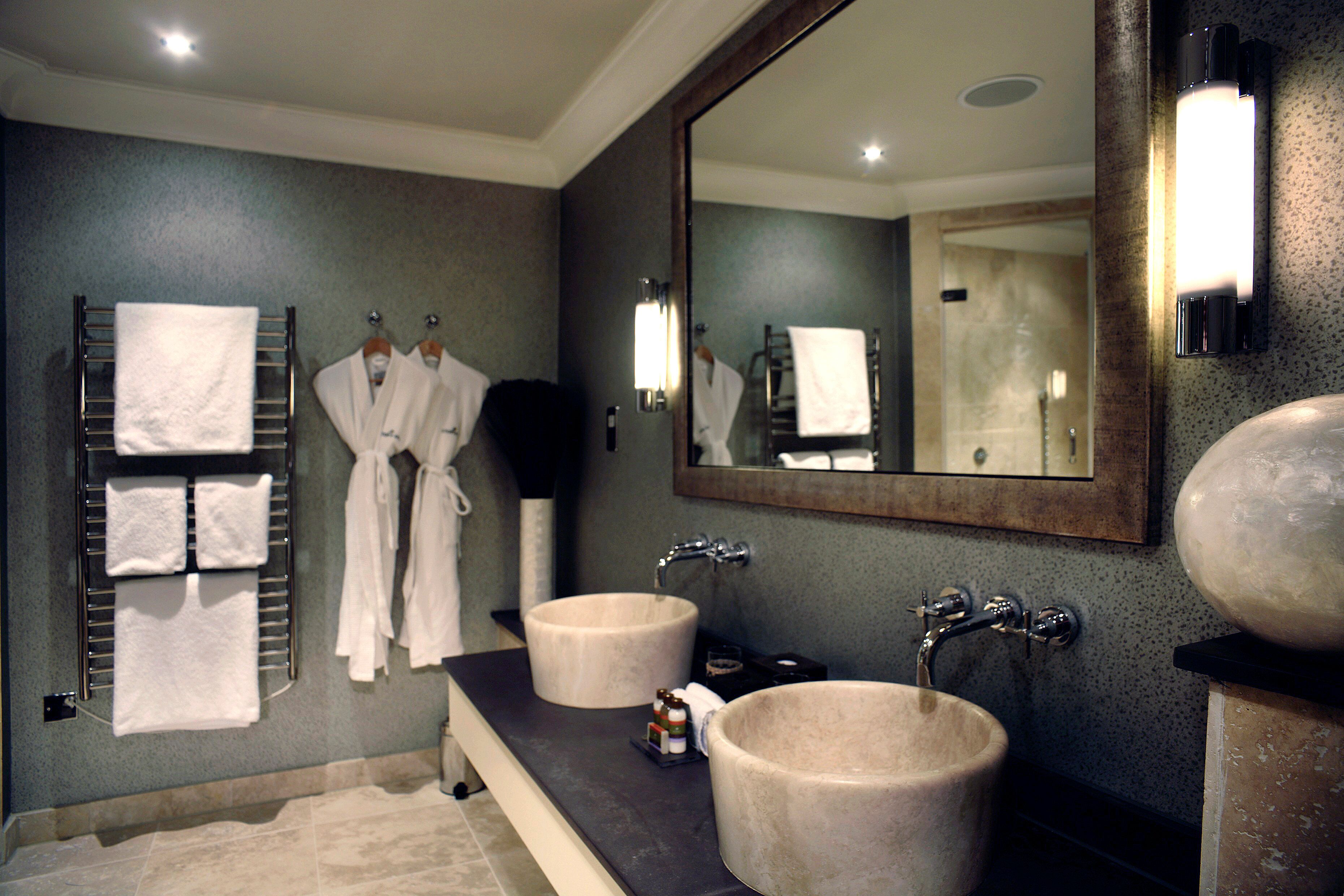 A bathroom with two sinks, a large mirror, and multiple towels and robes hanging on a rack.