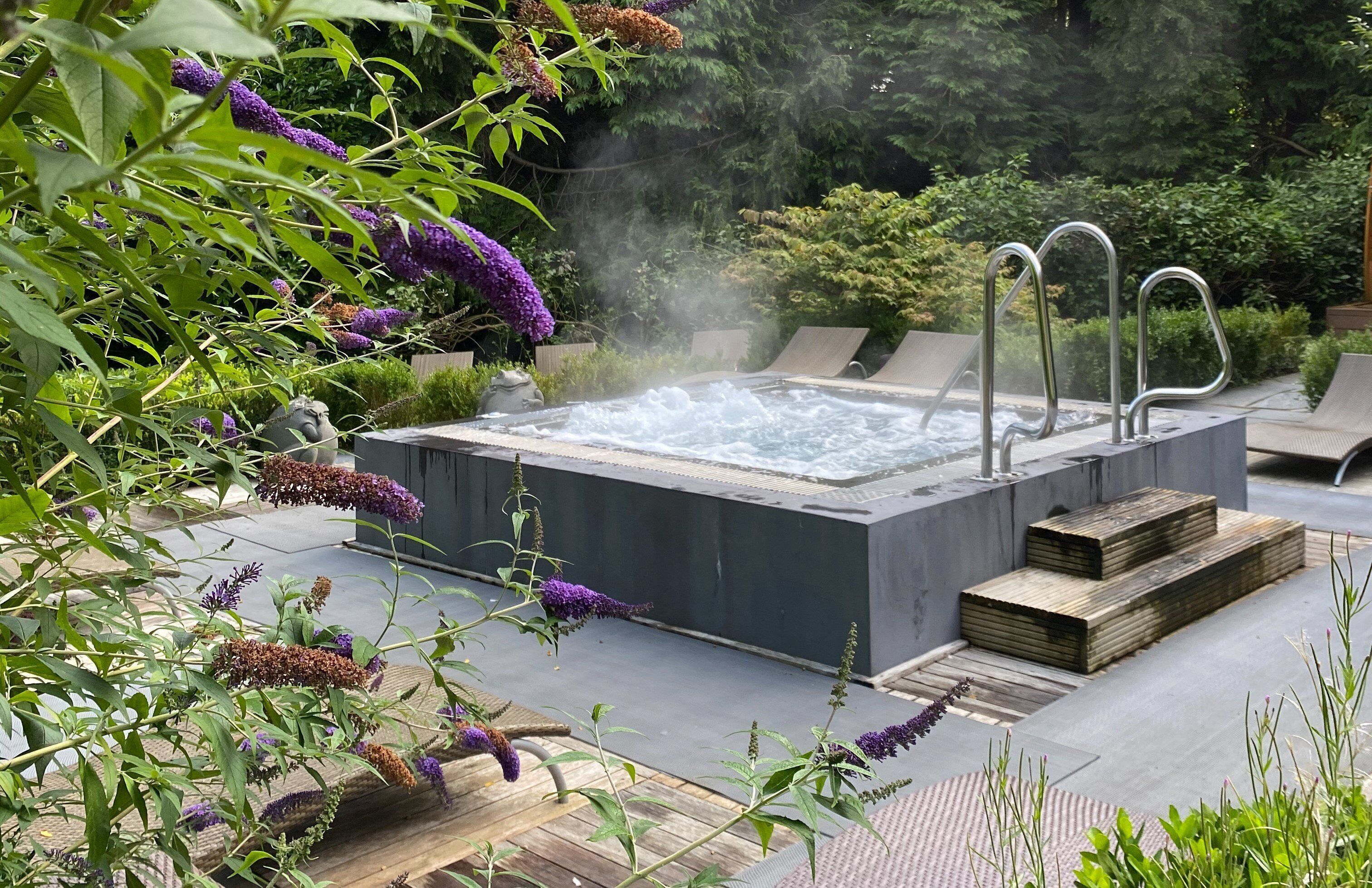 A hot tub surrounded by lush greenery and a wooden deck.